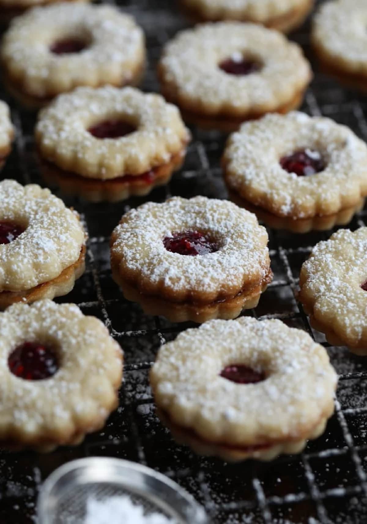 This is the absolute BEST Linzer Cookies recipe ever! These gorgeous and easy cookies are buttery, flaky shortbread filled with sweet jam and dusted with powdered sugar. A Christmas Cookie Classic! Linzer Cookies filled with strawberry jam dusted with powdered sugar on a wire rack