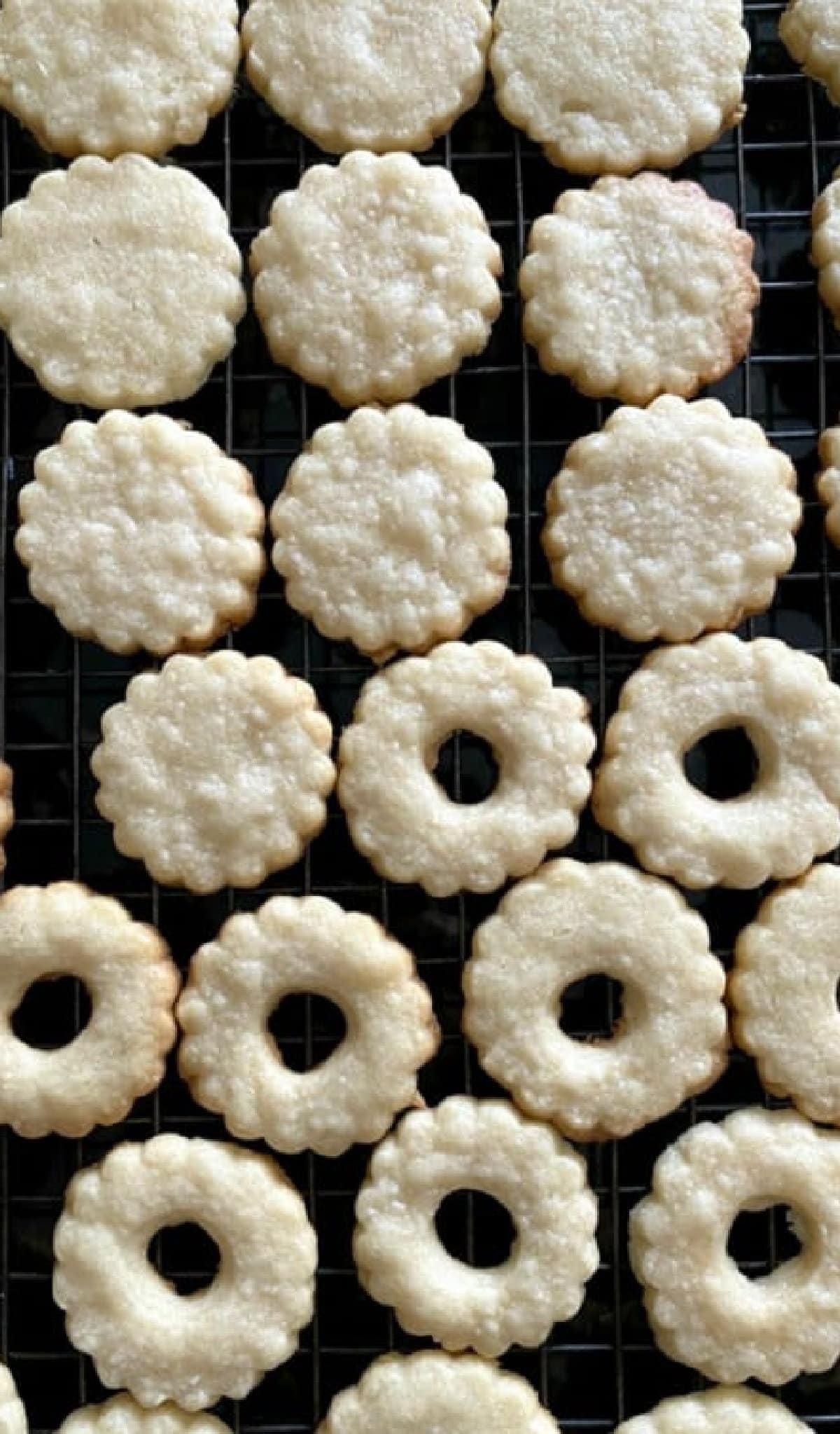 This is the absolute BEST Linzer Cookies recipe ever! These gorgeous and easy cookies are buttery, flaky shortbread filled with sweet jam and dusted with powdered sugar. A Christmas Cookie Classic! Cut our Linzer Cookies fresh out of the oven cooling on a wire rack