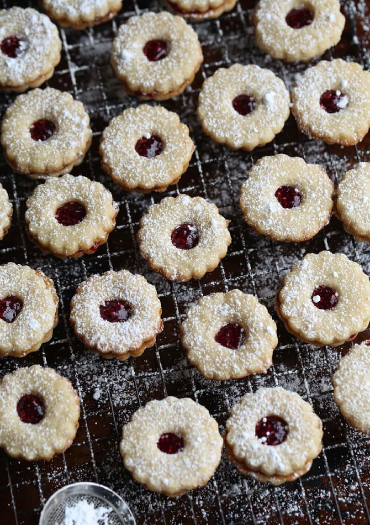 This is the absolute BEST Linzer Cookies recipe ever! These gorgeous and easy cookies are buttery, flaky shortbread filled with sweet jam and dusted with powdered sugar. A Christmas Cookie Classic! Linzer Cookies on a wire rack dusted with powdered sugar