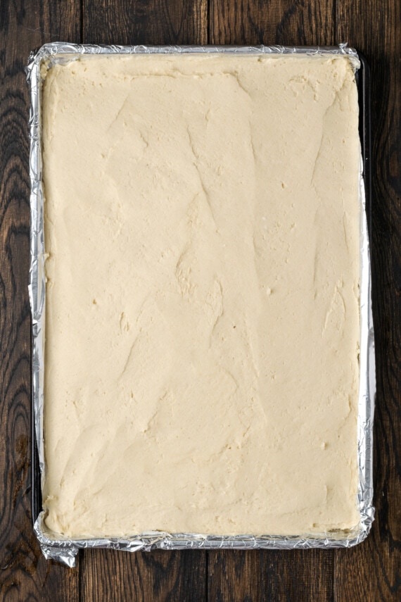 These soft and chewy frosted sugar cookie bars are topped with a thick layer of buttercream frosting (and sprinkles!). Ready in 30 minutes! Sugar cookie dough pressed into a lined baking pan.