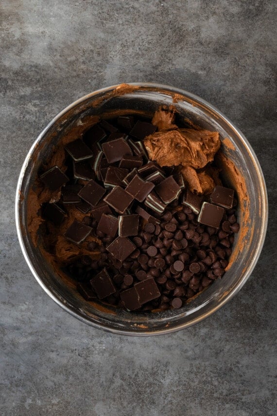 Chopped Andes mints and chocolate chips added to chccolate cookie dough in a metal bowl.