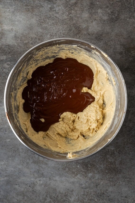 Melted chocolate added to creamed wet ingredients in a metal mixing bowl.