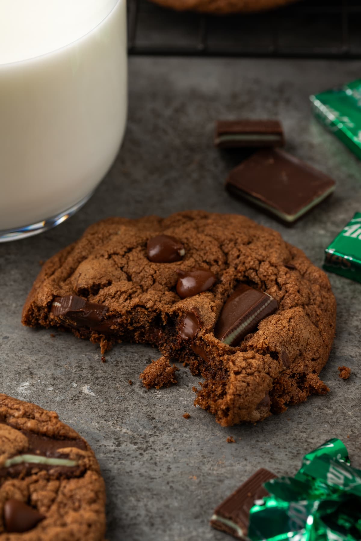 Close up of a double chocolate mint cookie with a bite missing, next to a glass of milk.