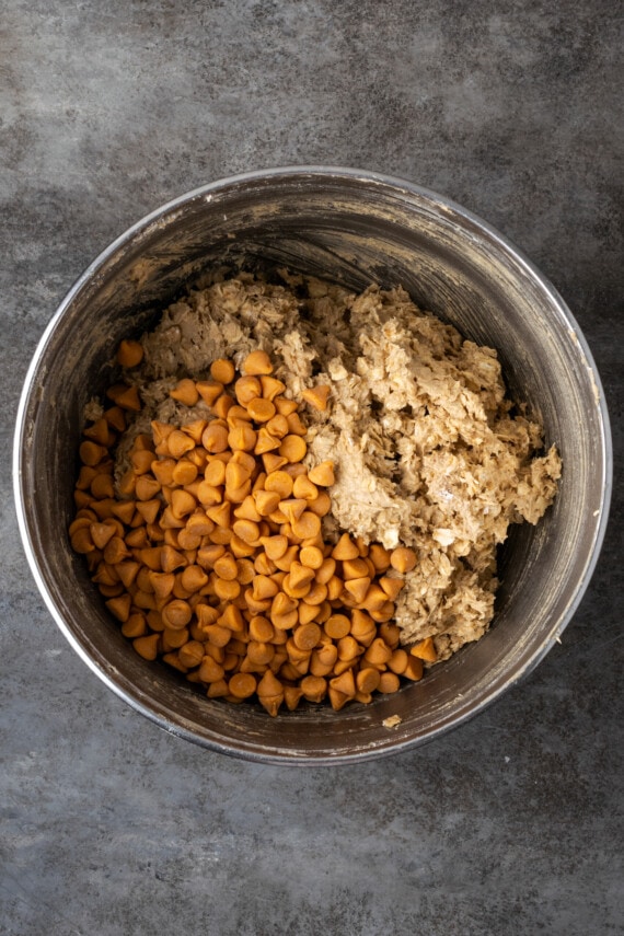 Soft and chewy oatmeal butterscotch cookies are rich and buttery, filled with tender oats, butterscotch morsels, and sweet cinnamon spice. Butterscotch chips added to oatmeal cookie dough in a metal mixing bowl.