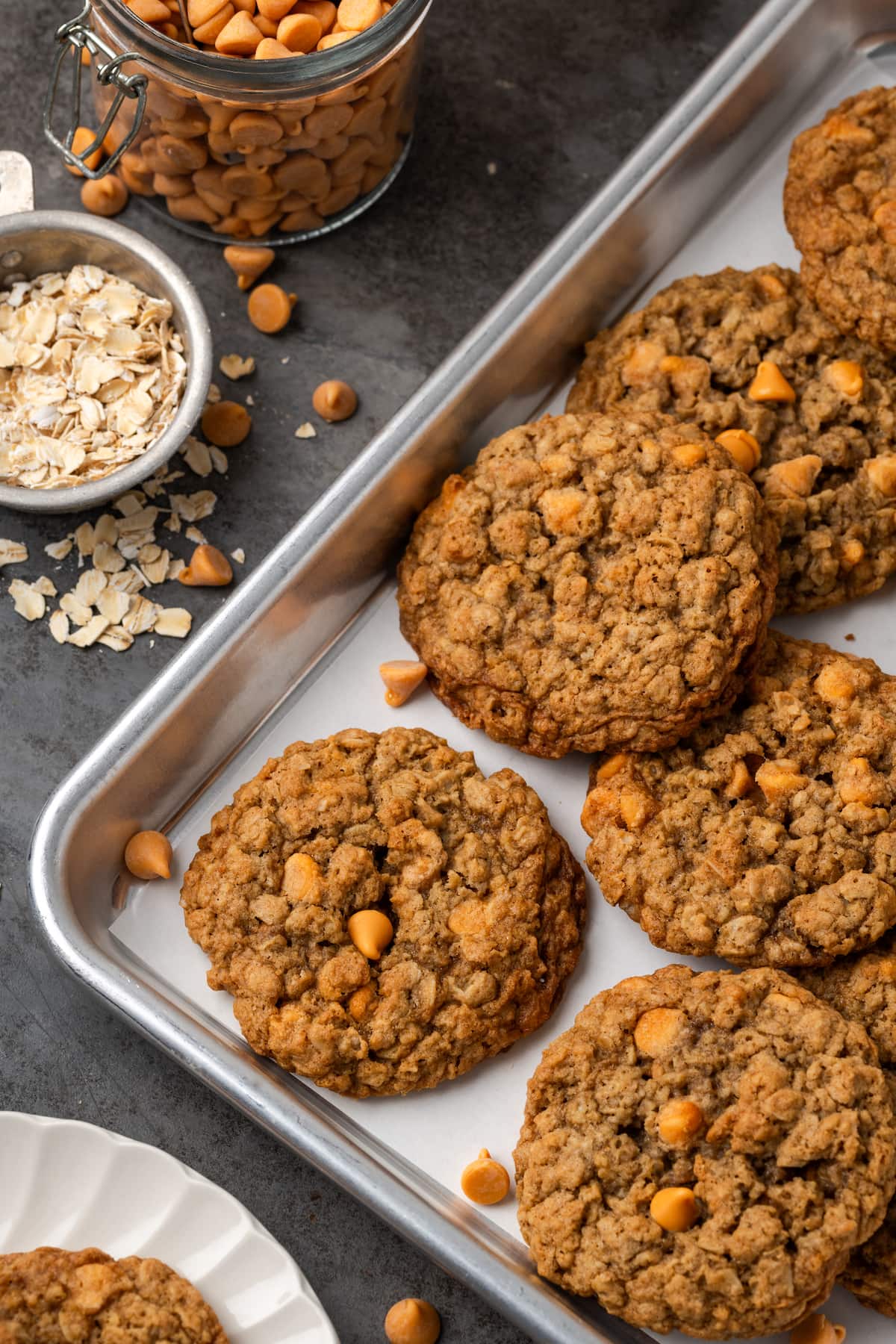 Soft and chewy oatmeal butterscotch cookies are rich and buttery, filled with tender oats, butterscotch morsels, and sweet cinnamon spice. Assorted oatmeal butterscotch cookies on a baking sheet, next to small bowls of oats and butterscotch chips.