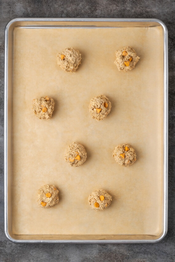 Soft and chewy oatmeal butterscotch cookies are rich and buttery, filled with tender oats, butterscotch morsels, and sweet cinnamon spice. Oatmeal butterscotch cookie dough balls on a parchment-lined baking sheet.