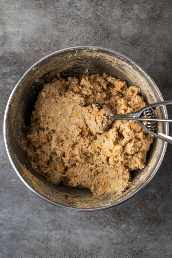 Soft and chewy oatmeal butterscotch cookies are rich and buttery, filled with tender oats, butterscotch morsels, and sweet cinnamon spice. Oatmeal butterscotch cookie dough in a metal mixing bowl, with a cookie scoop.