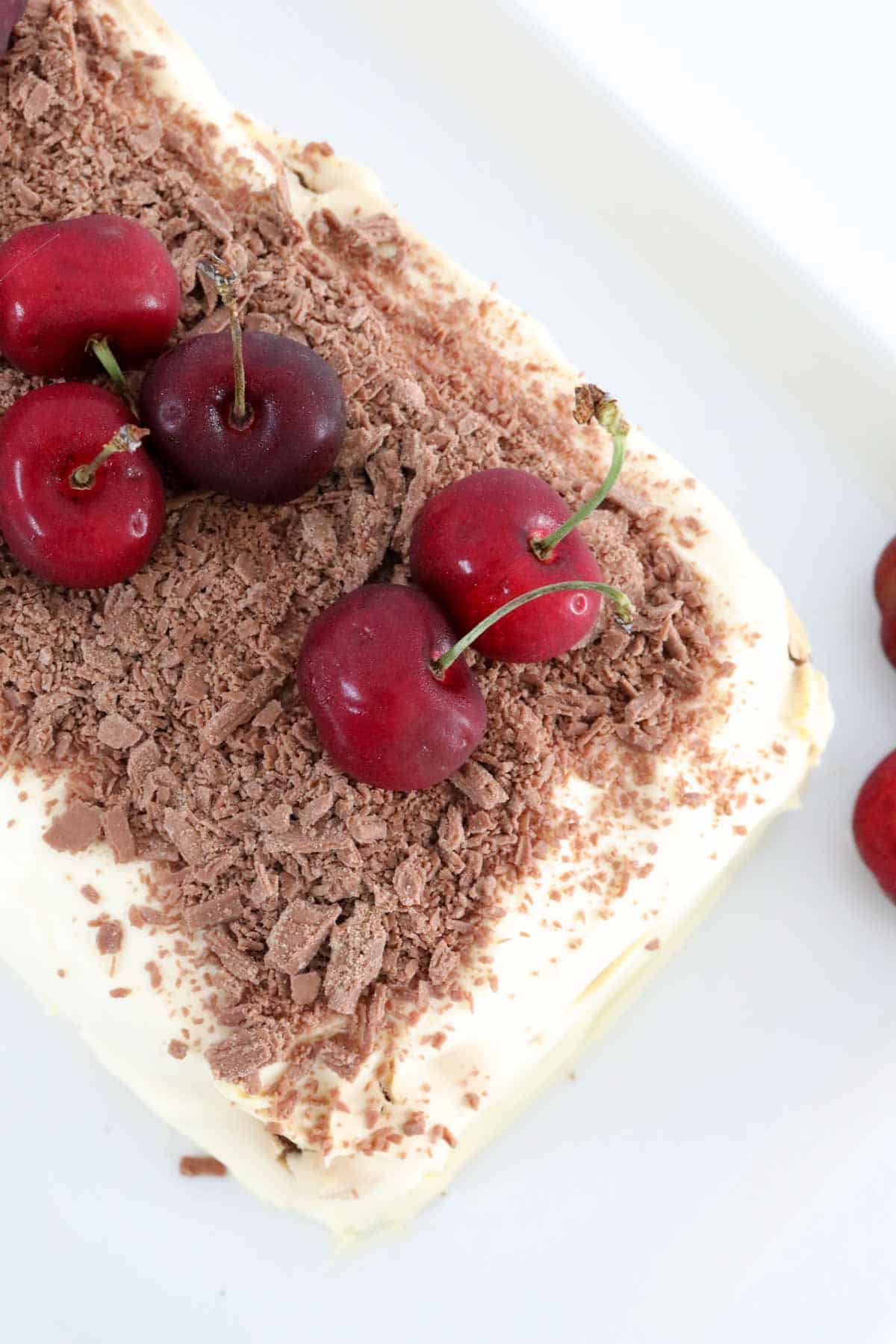 An overhead shot of cherries and chocolate on a whipped cream covered dessert.