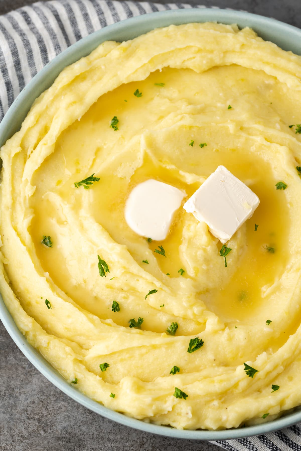 Buttery, fluffy Instant Pot Mashed Potatoes are a flavorful and easy side dish. Enjoy creamy homemade mashed potatoes, ready in half the time! Creamy Instant Pot mashed potatoes in a bowl topped with two pats of butter and chives.