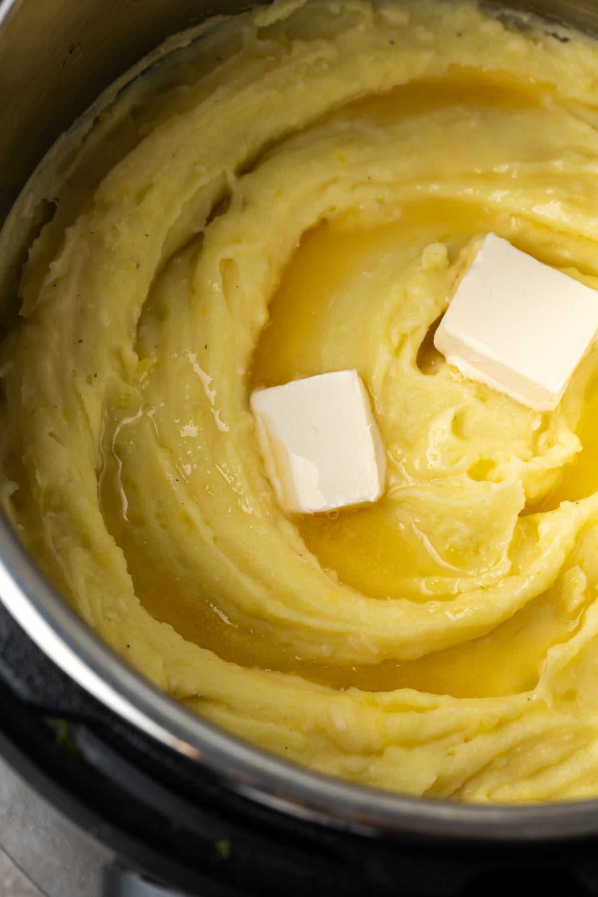 Buttery, fluffy Instant Pot Mashed Potatoes are a flavorful and easy side dish. Enjoy creamy homemade mashed potatoes, ready in half the time! Two pats of butter added to creamy mashed potatoes inside the Instant Pot.