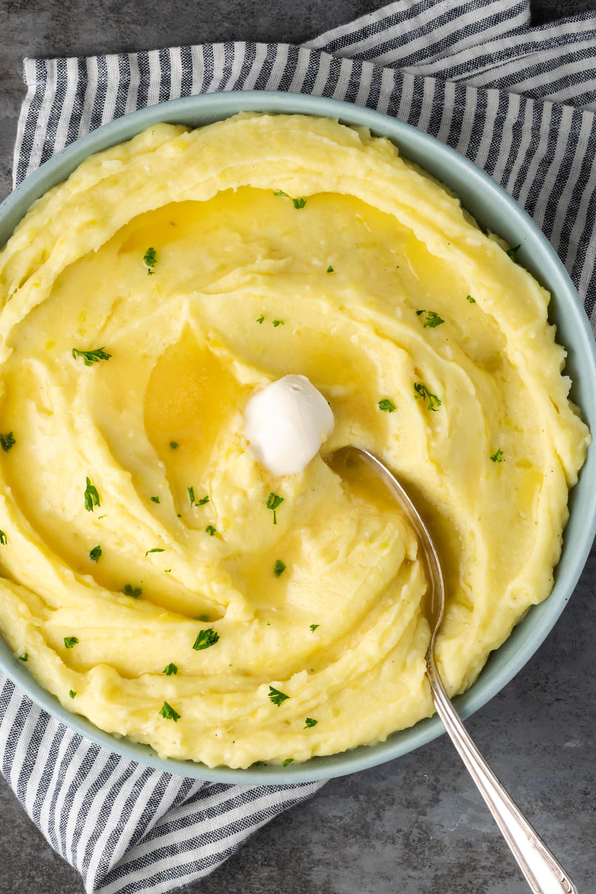 Buttery, fluffy Instant Pot Mashed Potatoes are a flavorful and easy side dish. Enjoy creamy homemade mashed potatoes, ready in half the time! A spoon stuck into a bowl of creamy Instant Pot mashed potatoes topped with butter.