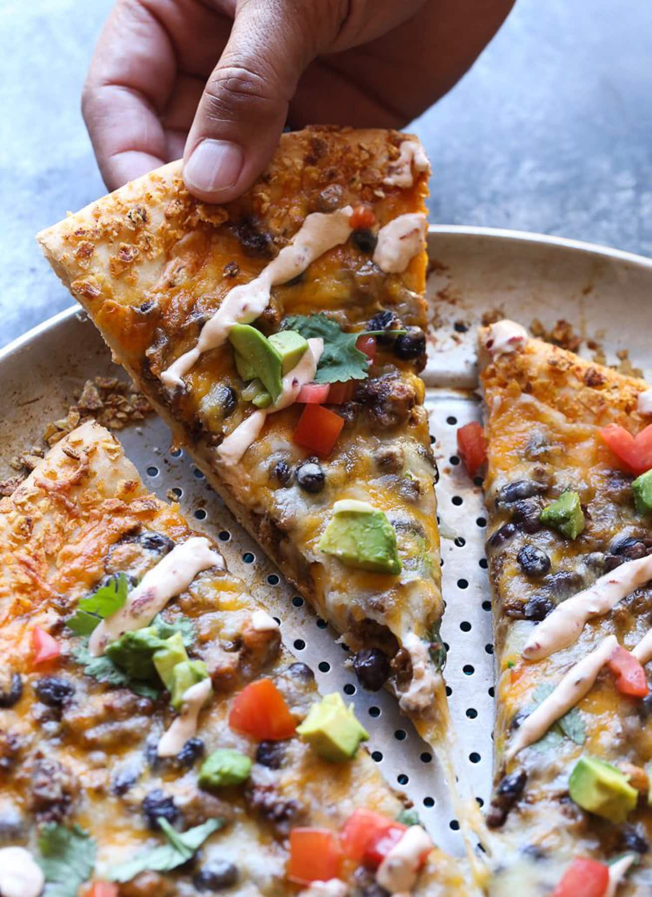 A hand lifts a slice of taco pizza from the rest of the pizza on a baking pan.