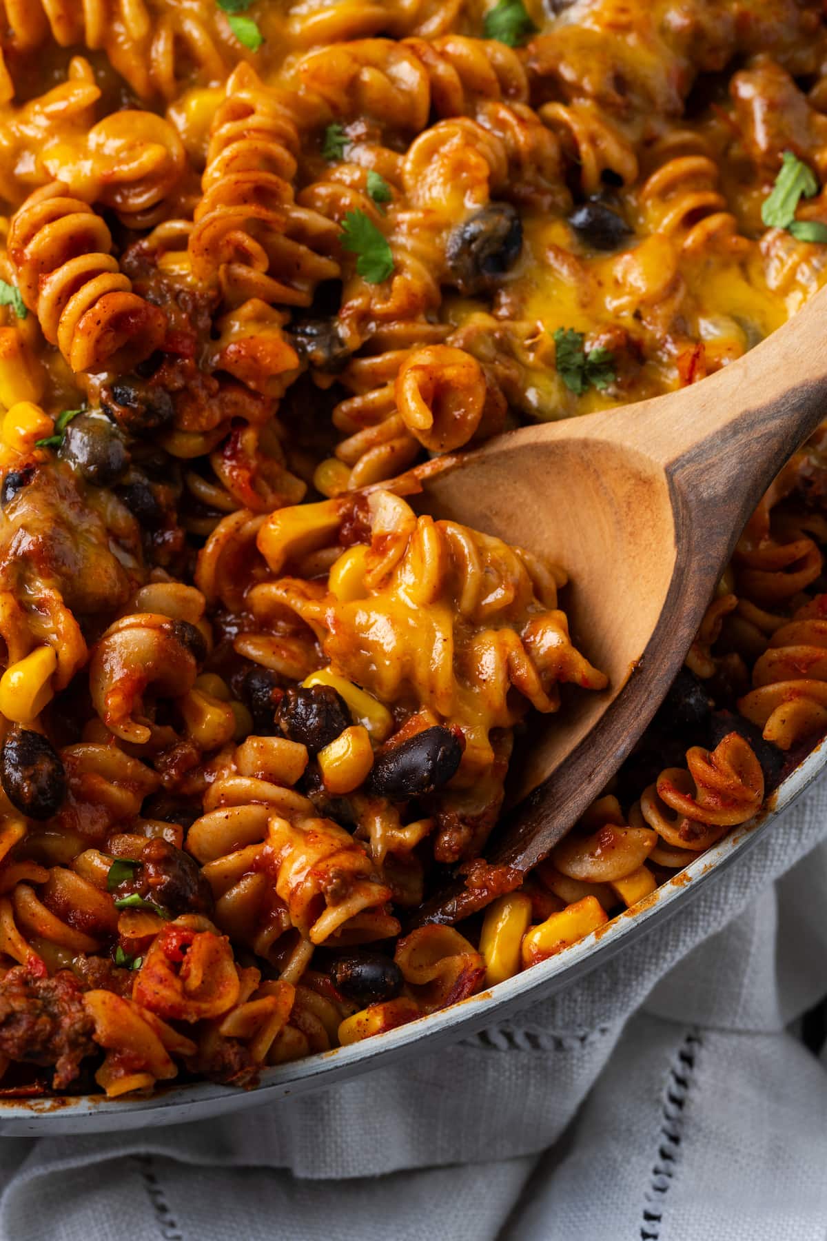 Close up of a wooden spoon stuck into a pan of cheesy taco pasta.