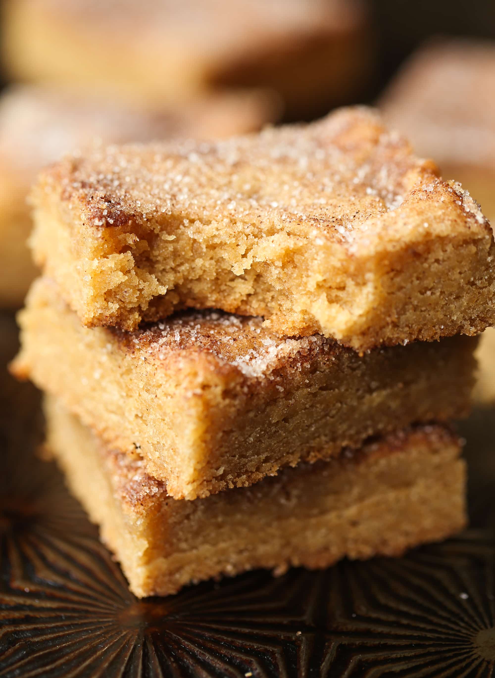 Buttery, chewy cookie bars that taste just like a churro! A stack of cinnamon sugar Churro cookie bars stacked with a bite taken from the top one.