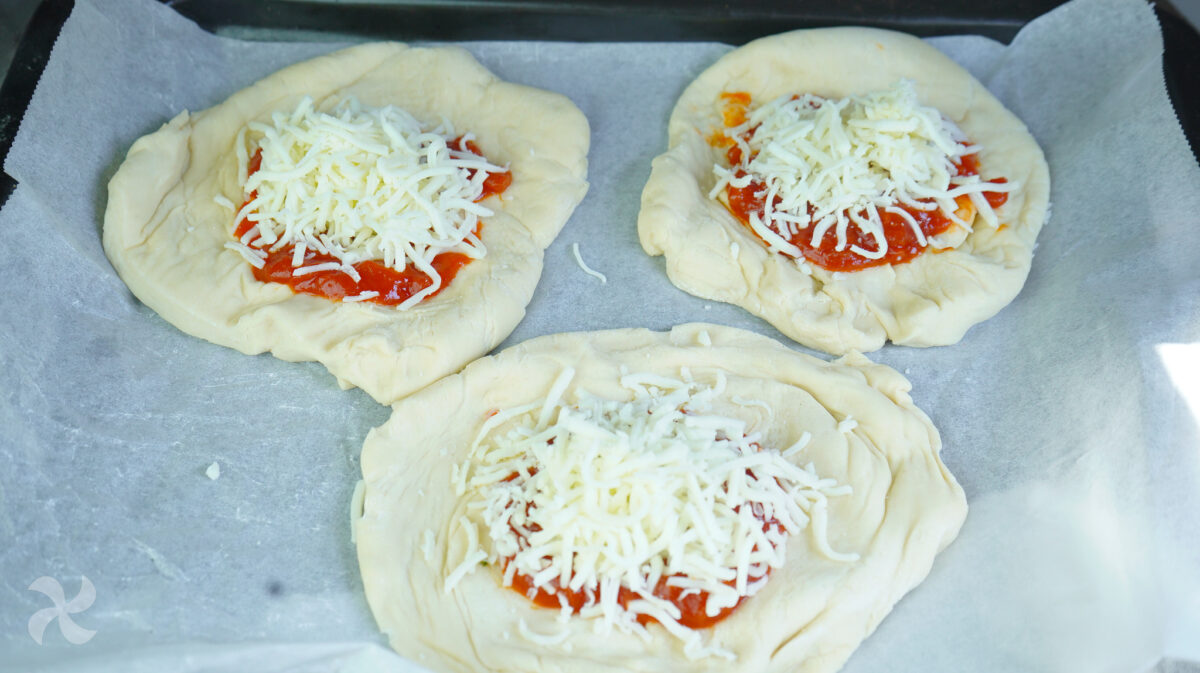 Hacemos mini pizzas y agregamos tomate y queso