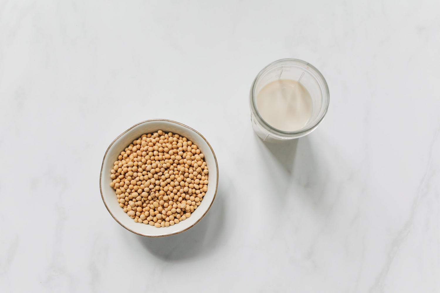 Cuenco con granos de soja y un vaso de leche de soja sobre una superficie de mármol blanco.