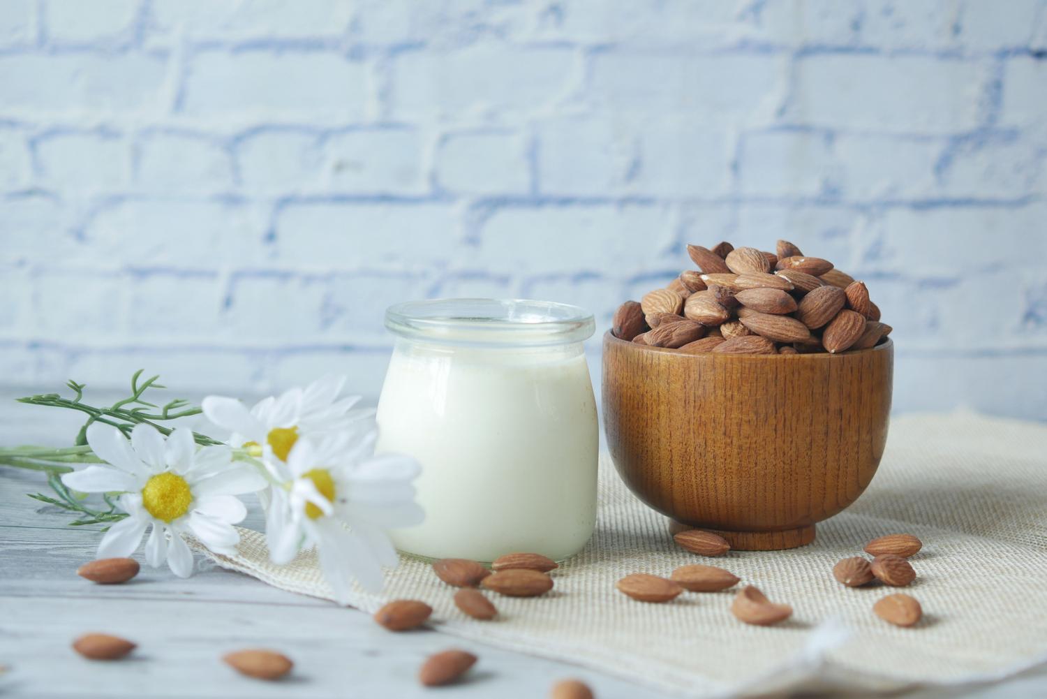 Almendras naturales en un cuenco de madera junto a un frasco de leche vegetal casera.