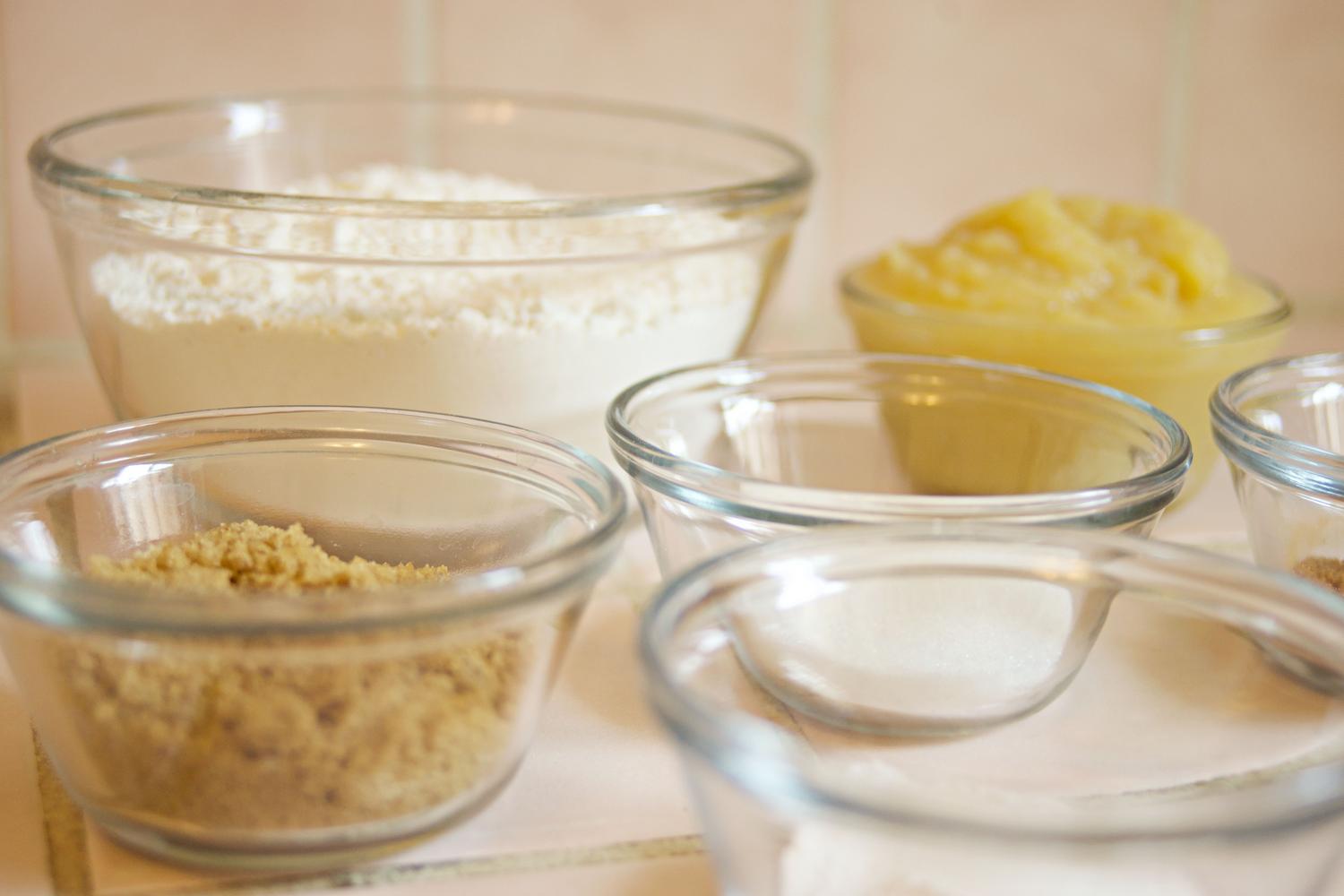 Ingredientes básicos de repostería, como azúcar y harina, organizados en cuencos de cristal.
