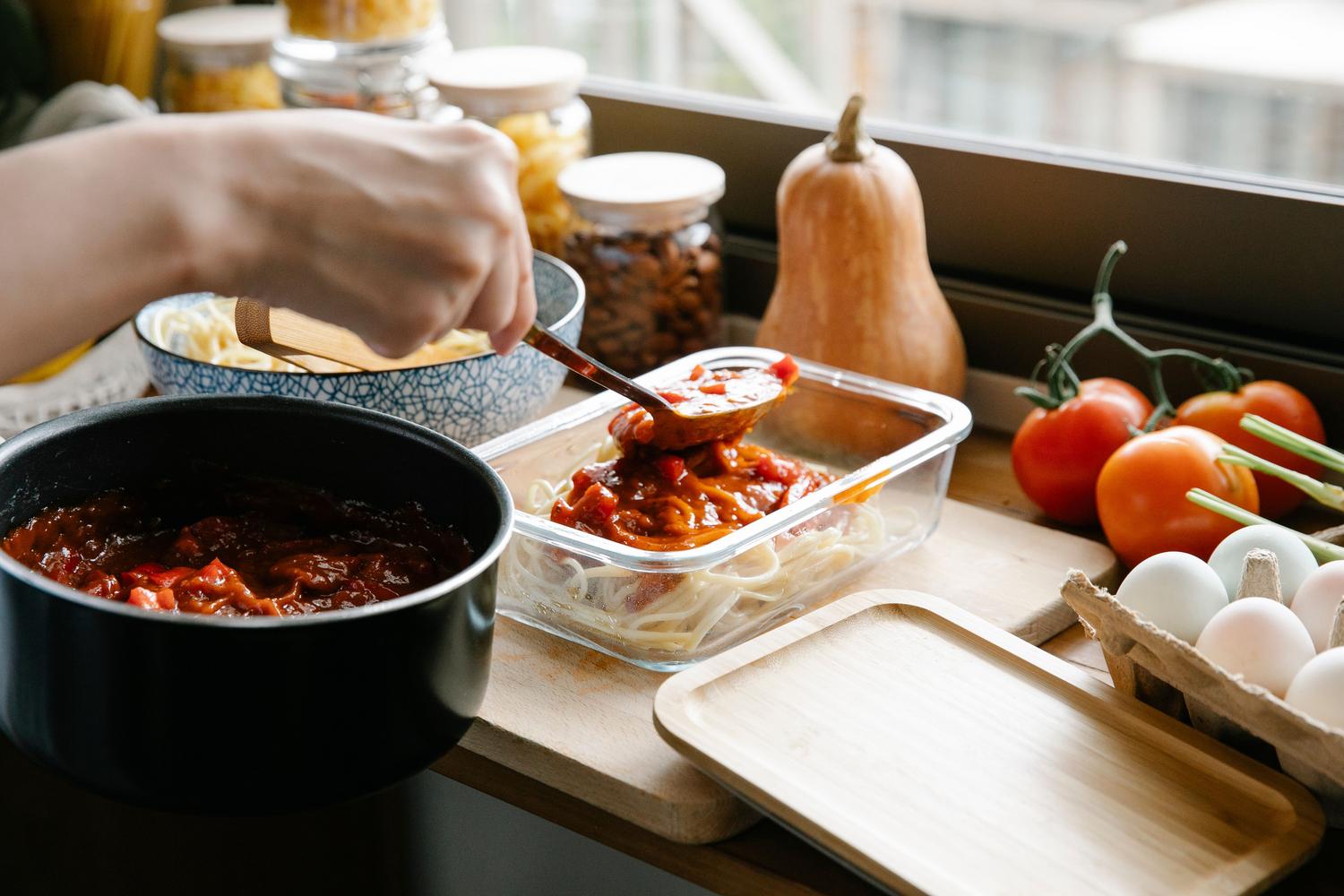 Proceso de servir salsa casera sobre pasta en un recipiente hermético para conservar la comida Proceso de servir salsa casera sobre pasta en un recipiente hermético para conservar la comida