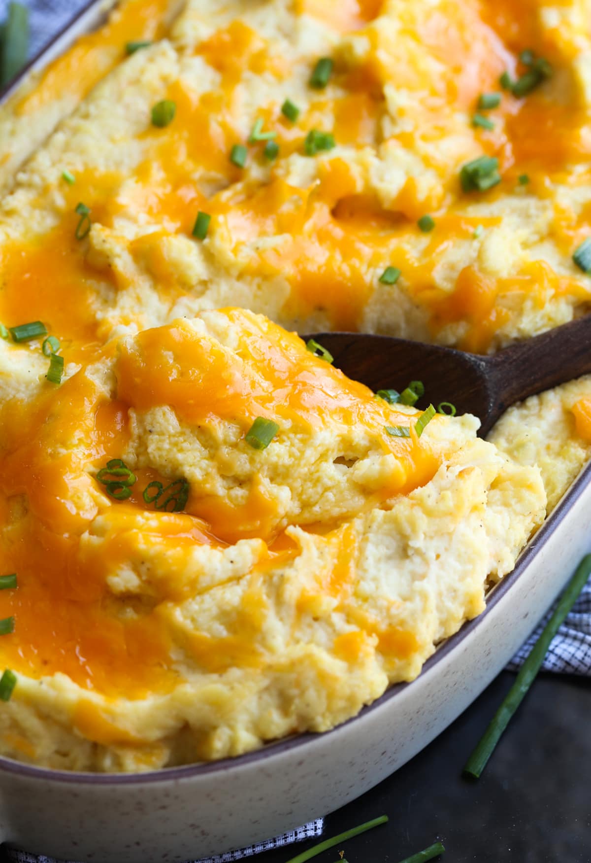 These Cheesy Baked Mashed Potatoes is the BEST mashed potato recipe ever! Cheese topped baked mashed potatoes with a wooden spoon to serve