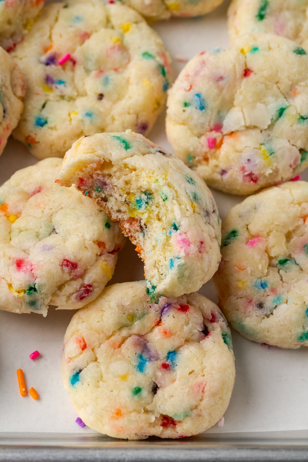 Close up of assorted funfetti cookies on a parchment-lined baking sheet, with a bite missing from one cookie.